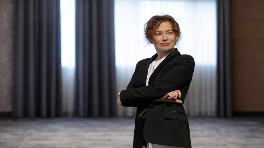 Portret editorial al Irinei Vincze, îmbrăcată într-un costum negru, surprinsă într-o postură calmă și sigură, cu brațele încrucișate, într-un spațiu interior sobru, sugerând reflecție și autoritate intelectuală.