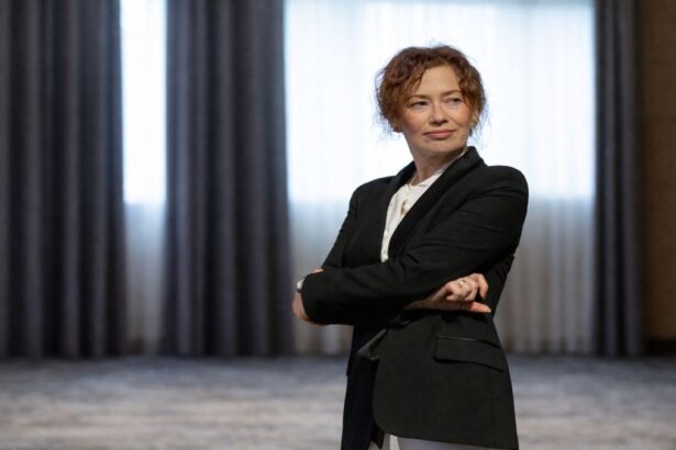 Portret editorial al Irinei Vincze, îmbrăcată într-un costum negru, surprinsă într-o postură calmă și sigură, cu brațele încrucișate, într-un spațiu interior sobru, sugerând reflecție și autoritate intelectuală.