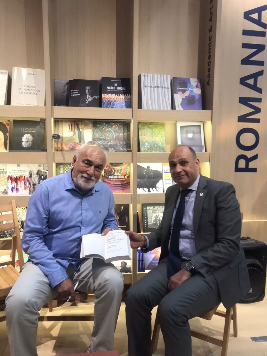 Amr Yehia and Varujan Vosganian seated at the Romanian Pavilion, holding a bilingual poetry anthology, during the Cairo International Book Fair.