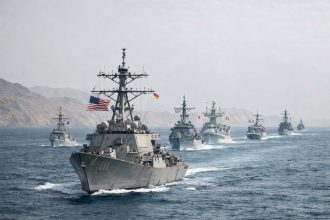 Allied naval vessels and commercial oil tankers in the Strait of Hormuz during the 2026 Gulf crisis, with flags of coalition member states represented among the warships present in the waterway