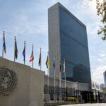 Sediul Organizației Națiunilor Unite din New York, cu sigla ONU și steagurile statelor membre.