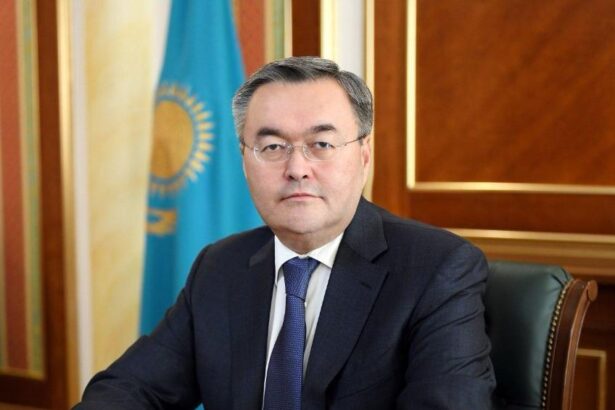 Mukhtar Tileuberdi seated beside Kazakhstan’s national flag.